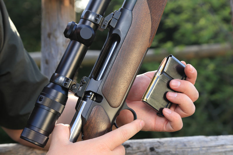 Hunter loading a magazine clip into a scoped hunting rifle