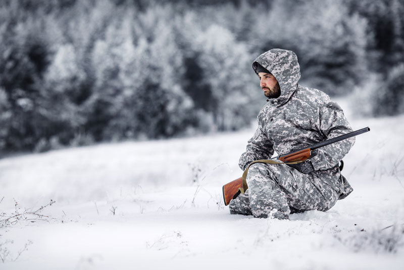 Hunter crouched in white camo attire in winter