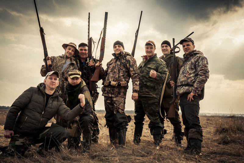 Group of eight hunters standing together against sunrise sky in rural field during hunting season