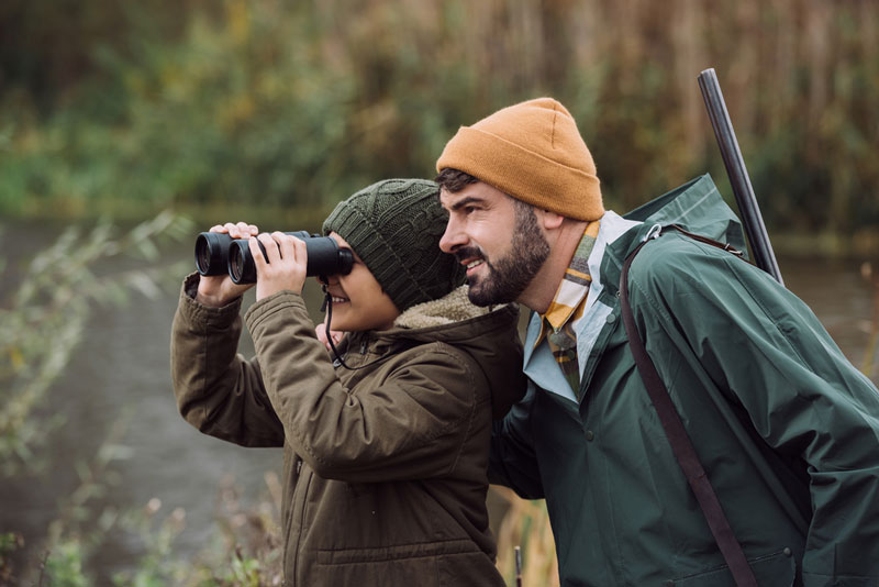 Father and son hunting while son looks through binoculars