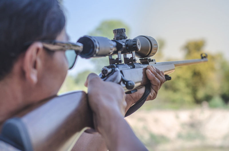 Man taking aim through rifle scope while target shooting