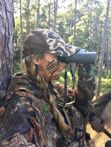 Female hunter in camo looking through binoculars