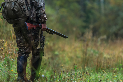 Man in camo standing with rifle near woods