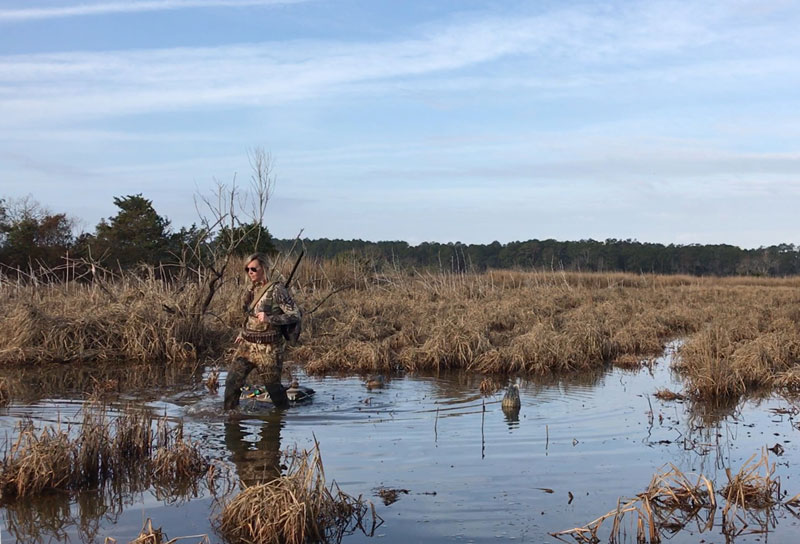 Woman in camo walking through swamp looking to pickup a decoy