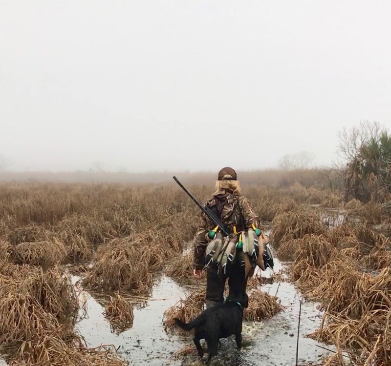 Woman with dog walking through field on duck hunt