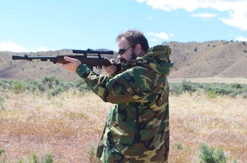 Author in camo jacket taking aim with a top hunting rifle