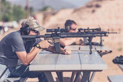 man firing a black rifle in desert