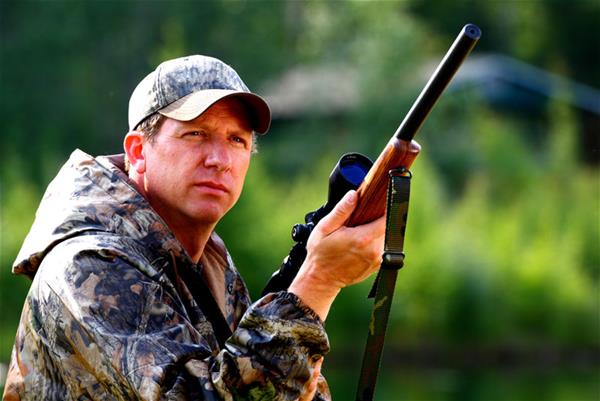 Hunter in camo outfit holding rifle preparing to shoot