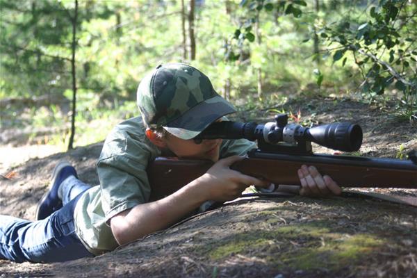 Teenage boy in camo laying on ground preparing to shoot rifle