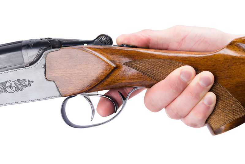Hand holding shotgun with finger on the trigger