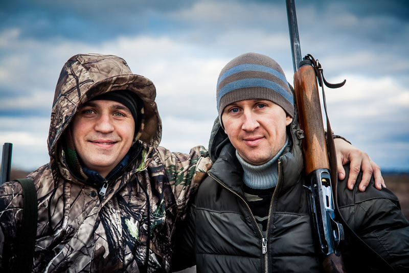 Friends standing together in front of dramatic sky on an overcast day during hunting season embracing each other