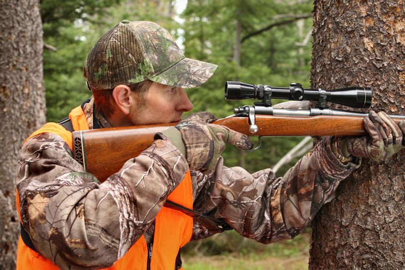 Deer hunter aiming rifle in woods
