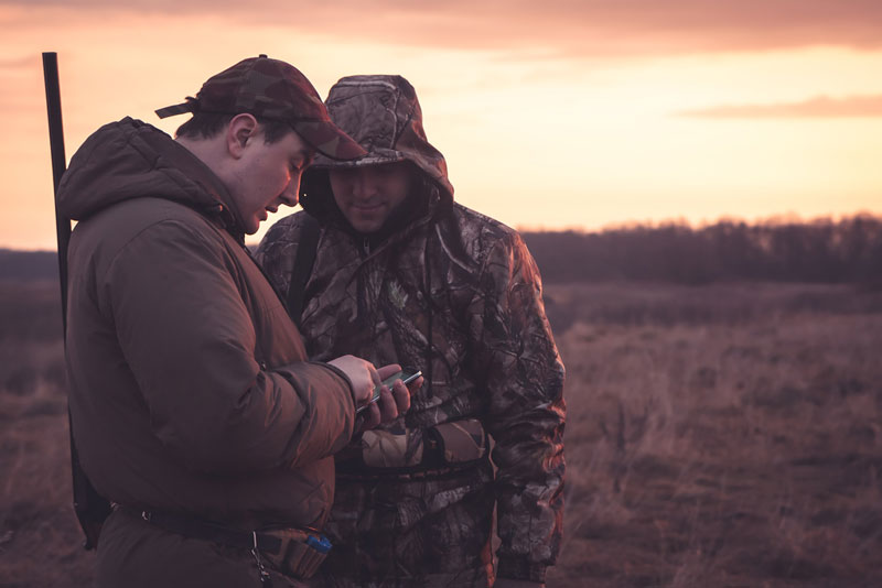 Two hunters in field looking at smart phone